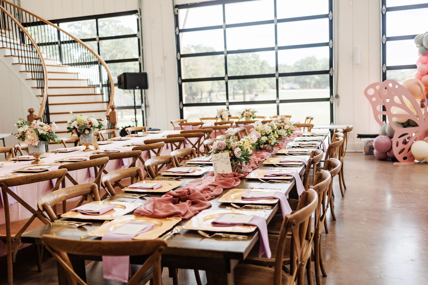 A first birthday party setup with wooden tables decorated with pink floral centerpieces at Bella Cavalli