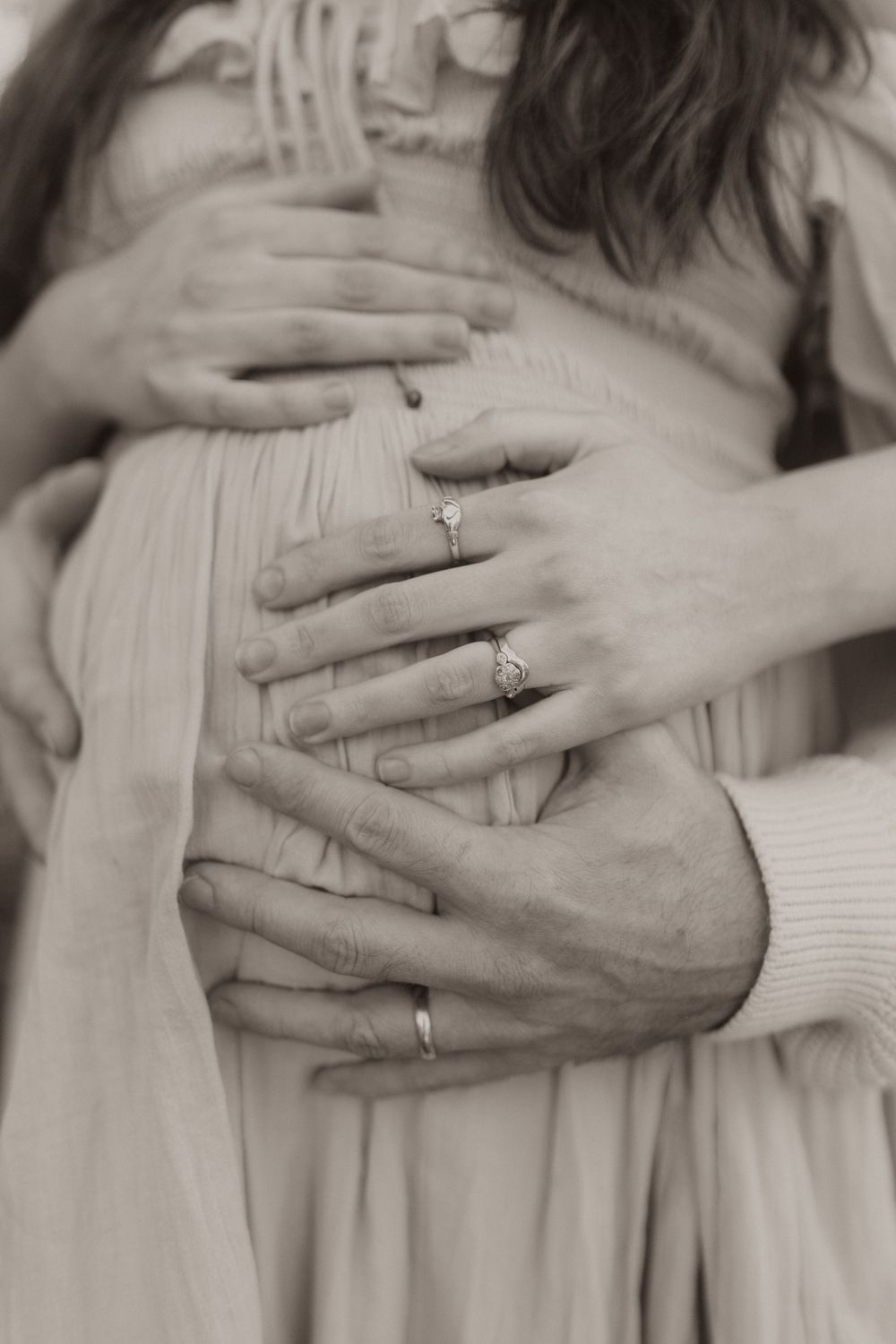 Close-up of intertwined hands with wedding rings resting against a sweater in black and white.