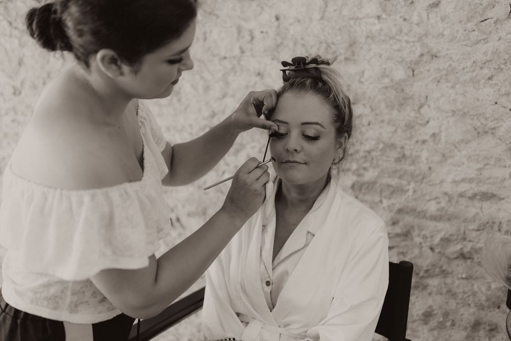 A makeup artist applies cosmetics to someone wearing a white robe during a wedding preparation session.