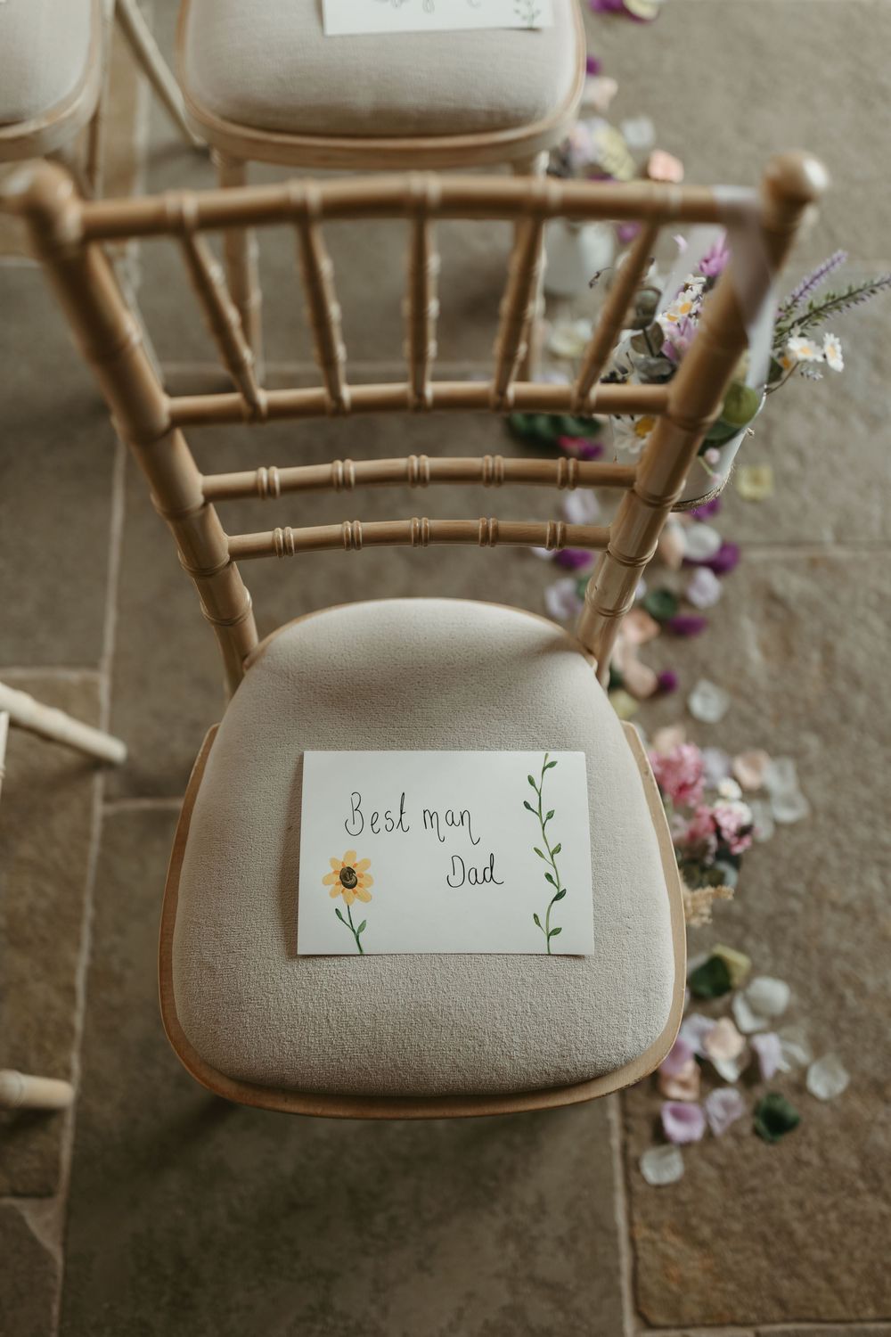 Wooden chair with a handwritten name card and floral decorations at a wedding venue.