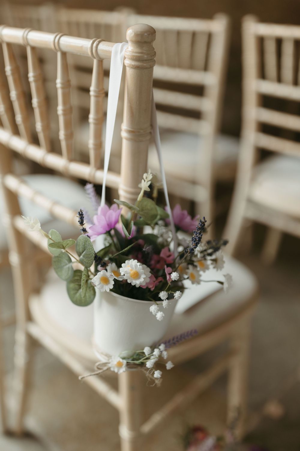 Delicate white chiavari chair decorated with a hanging white pot of purple and white wildflowers at a wedding ceremony.