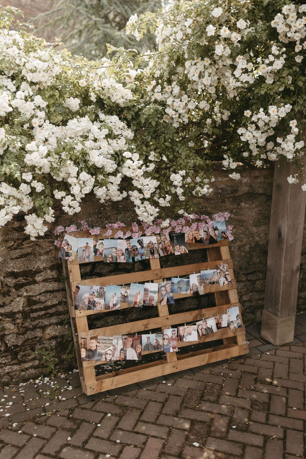 Rustic wooden pallet display wall decorated with wedding photos and climbing white flowers.