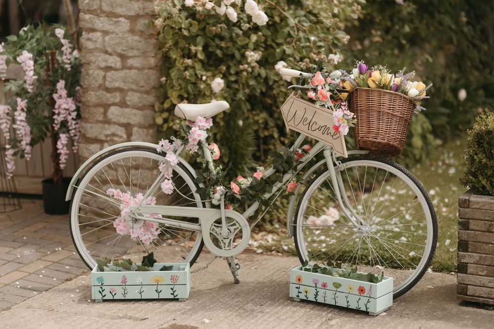 Vintage bicycle decorated with pink flowers and baskets against a brick wall.