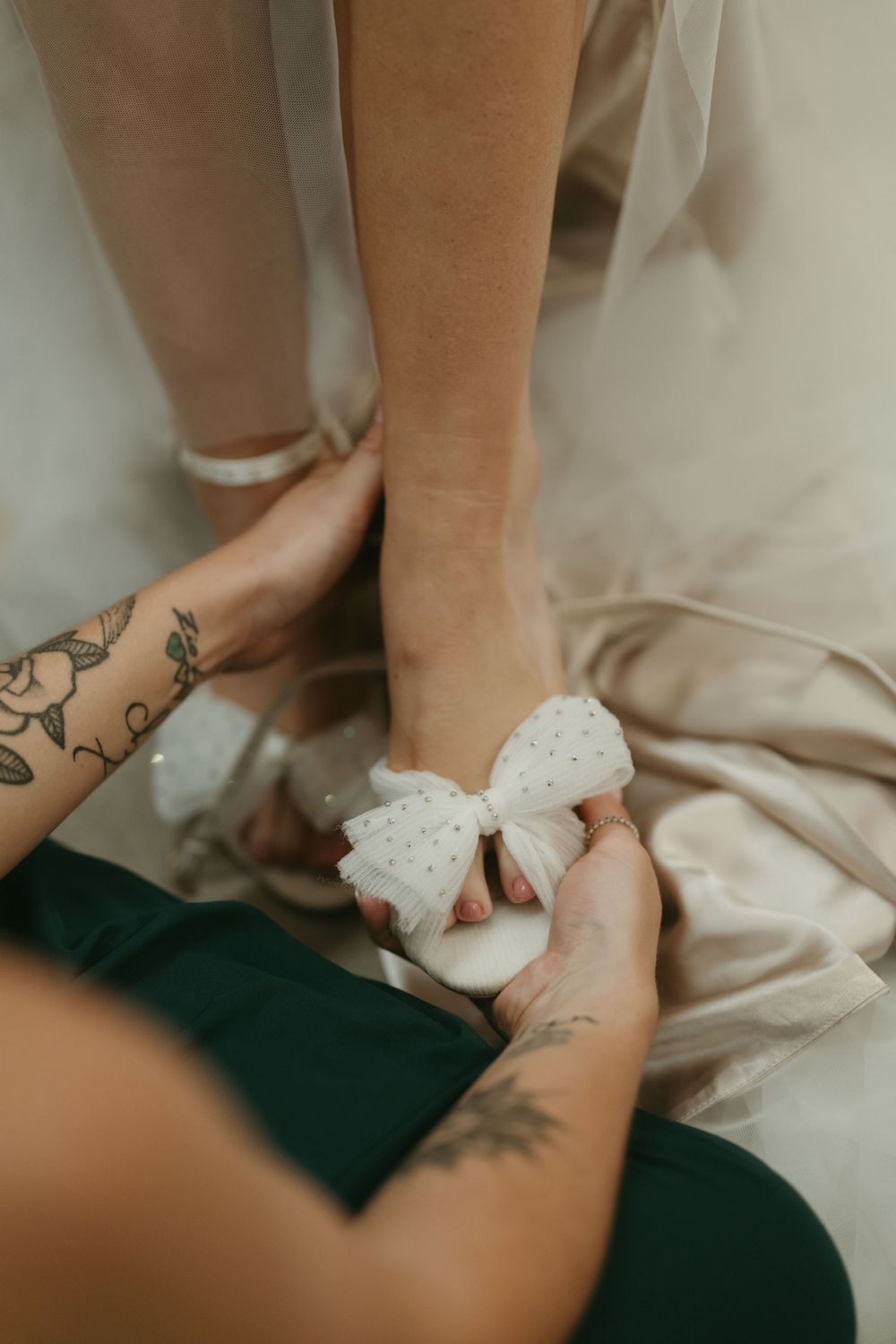 Close-up of tattooed hands adjusting a white bow detail on bridal shoes.