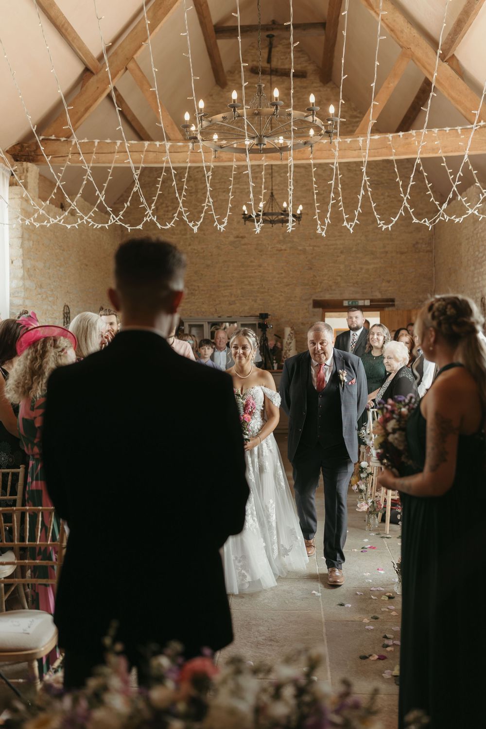 Wedding ceremony in a rustic barn venue with twinkling fairy lights strung across wooden beams.