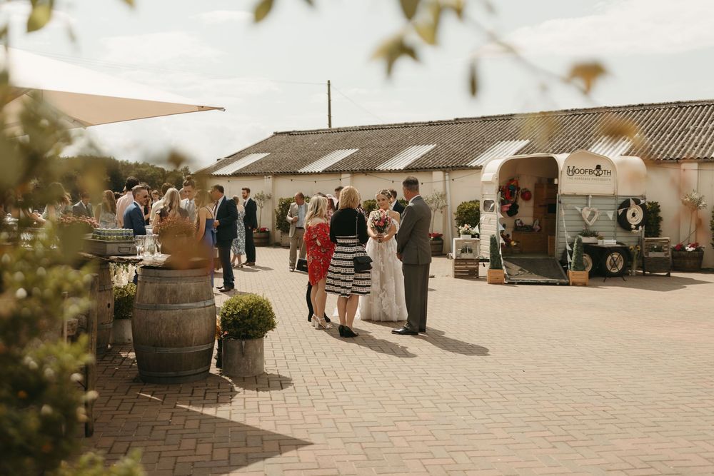 Wedding guests mingling outside a rustic venue with wine barrels and cobblestone courtyard.