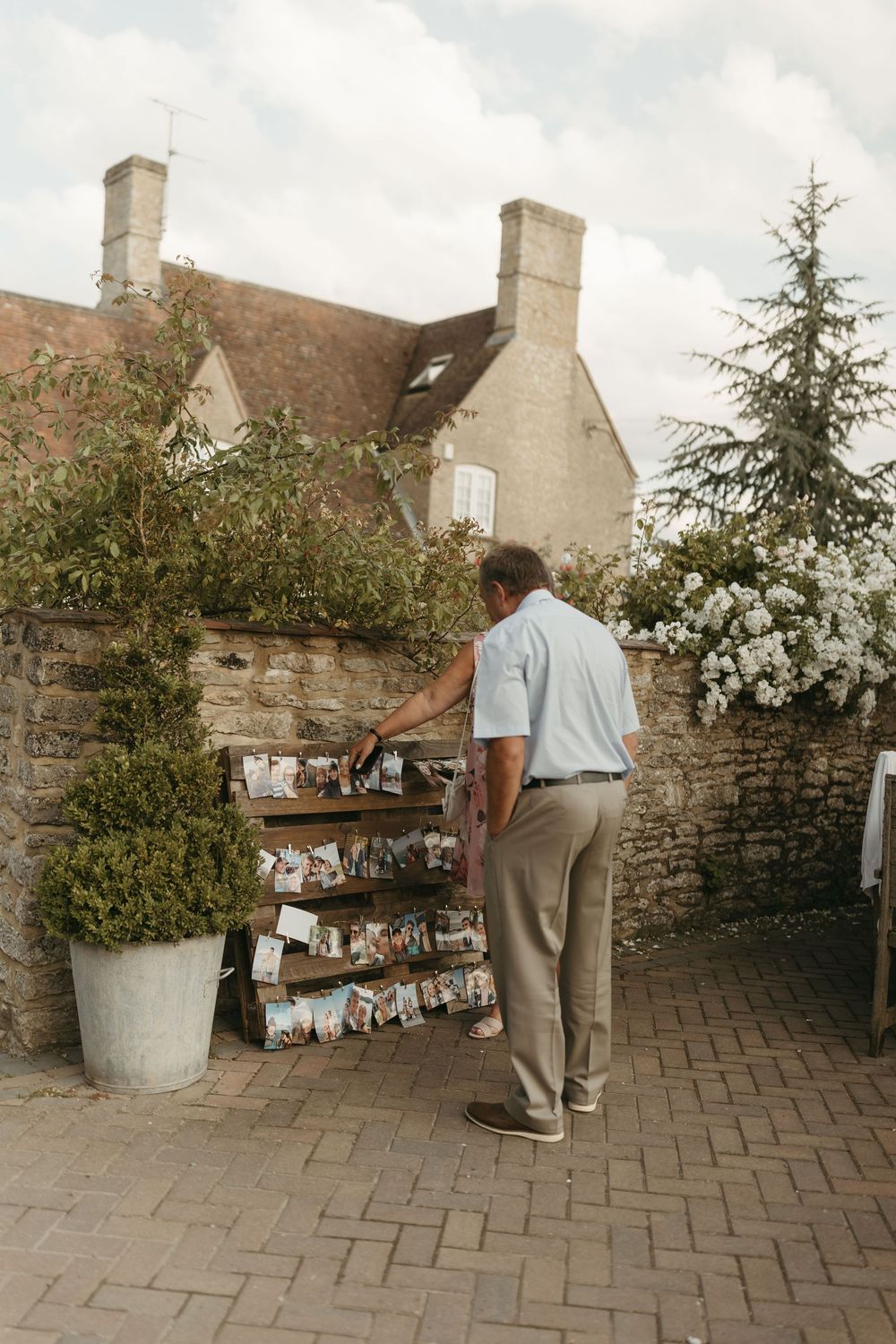 A person examining photo displays arranged on a rustic stone wall outside a classic English cottage.