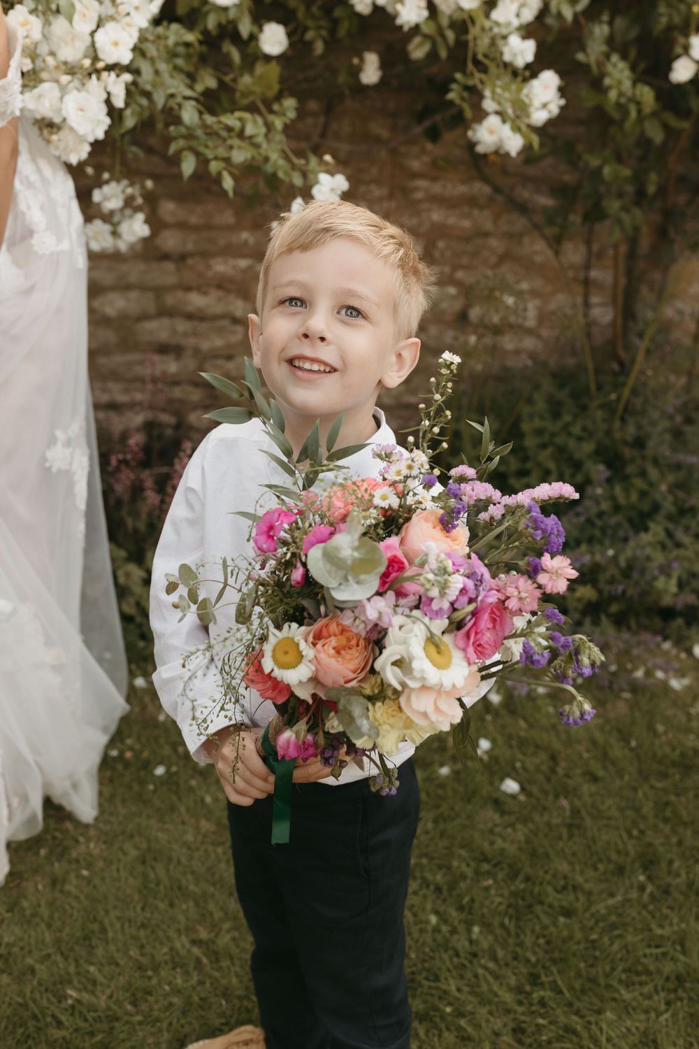 Young attendant in white shirt holding colorful wedding bouquet in garden setting.