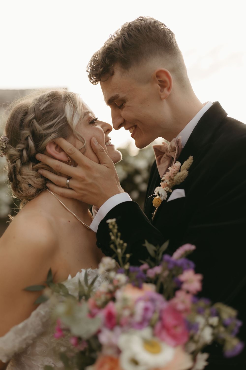 An intimate wedding moment captured during golden hour with purple and pink floral bouquet details.