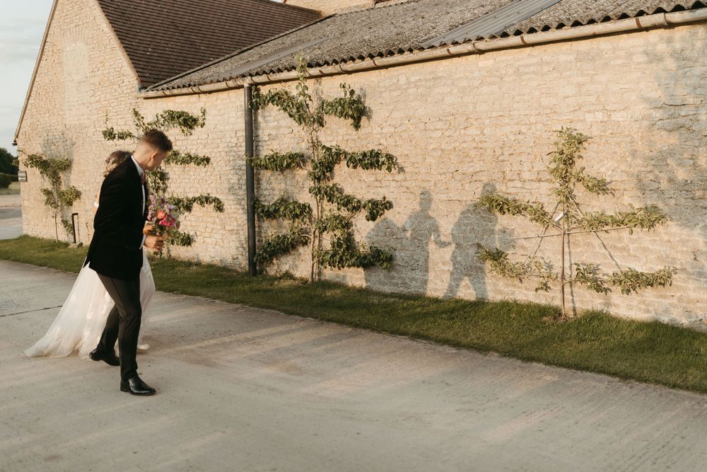 Wedding couple walking along a sunlit brick wall with climbing vines.