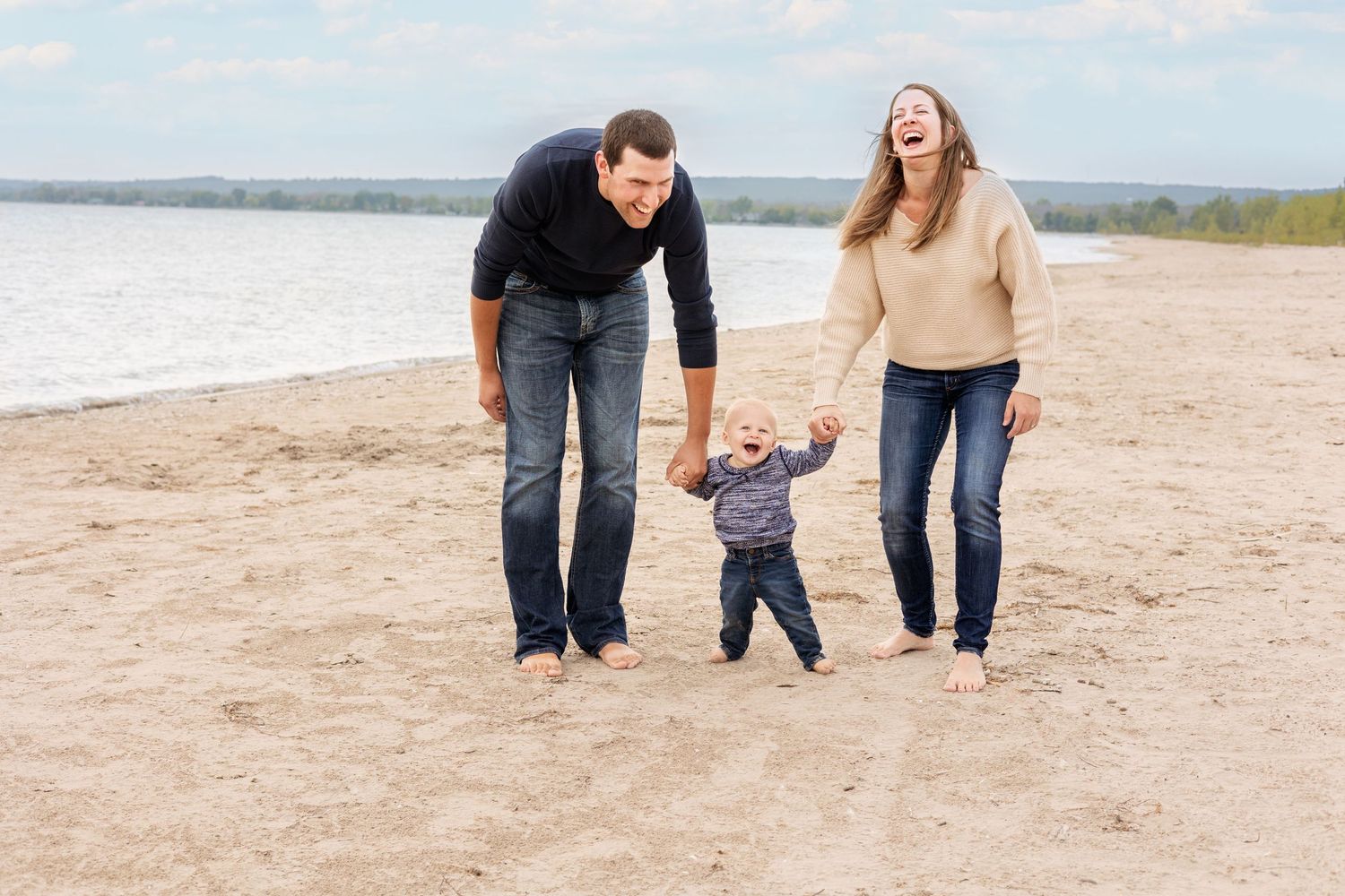 A family walks together while holding hands on a sandy beach during a winter day.