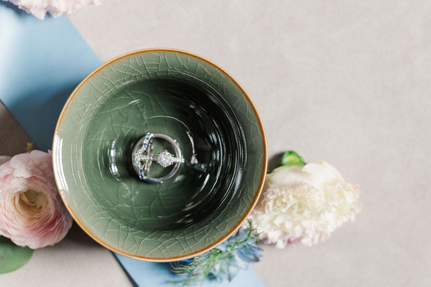 Overhead view of an empty green ceramic bowl with flowers on a light gray surface.