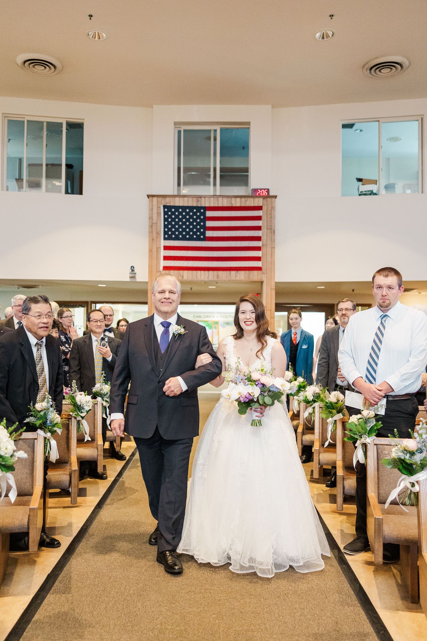 A traditional wedding ceremony in a church sanctuary with wooden pews and an American flag displayed prominently on the wall.