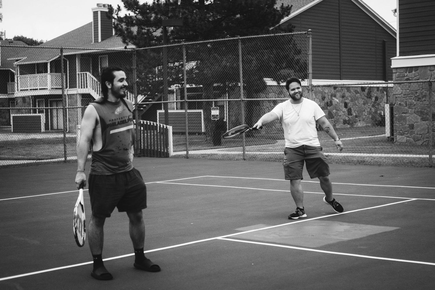 Two players engaged in a tennis match on an outdoor court, captured in black and white.