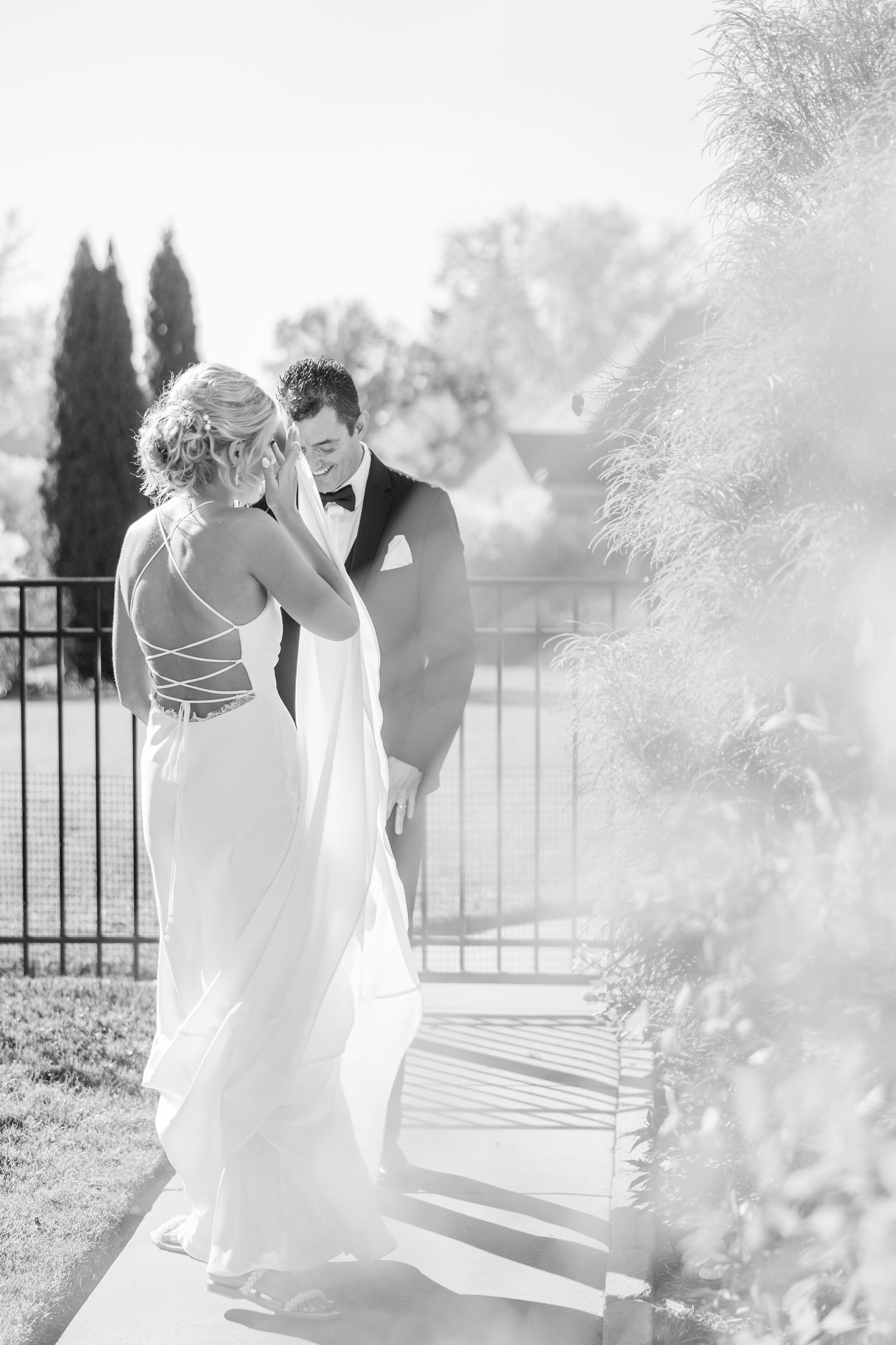 An elegant black and white wedding photo captured in a sun-drenched garden setting.