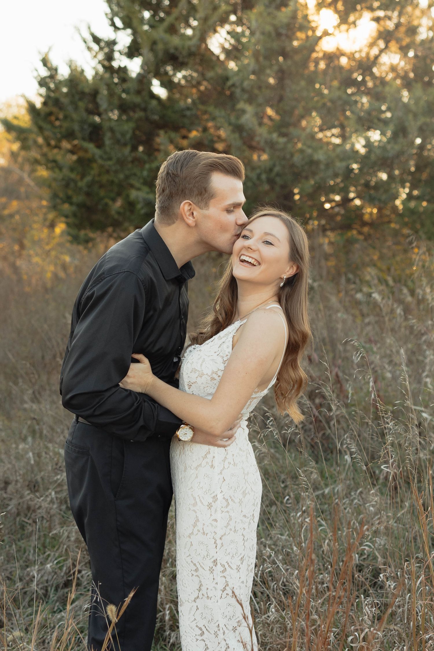 Couple embraces in golden sunlit field during romantic outdoor sunset photoshoot.