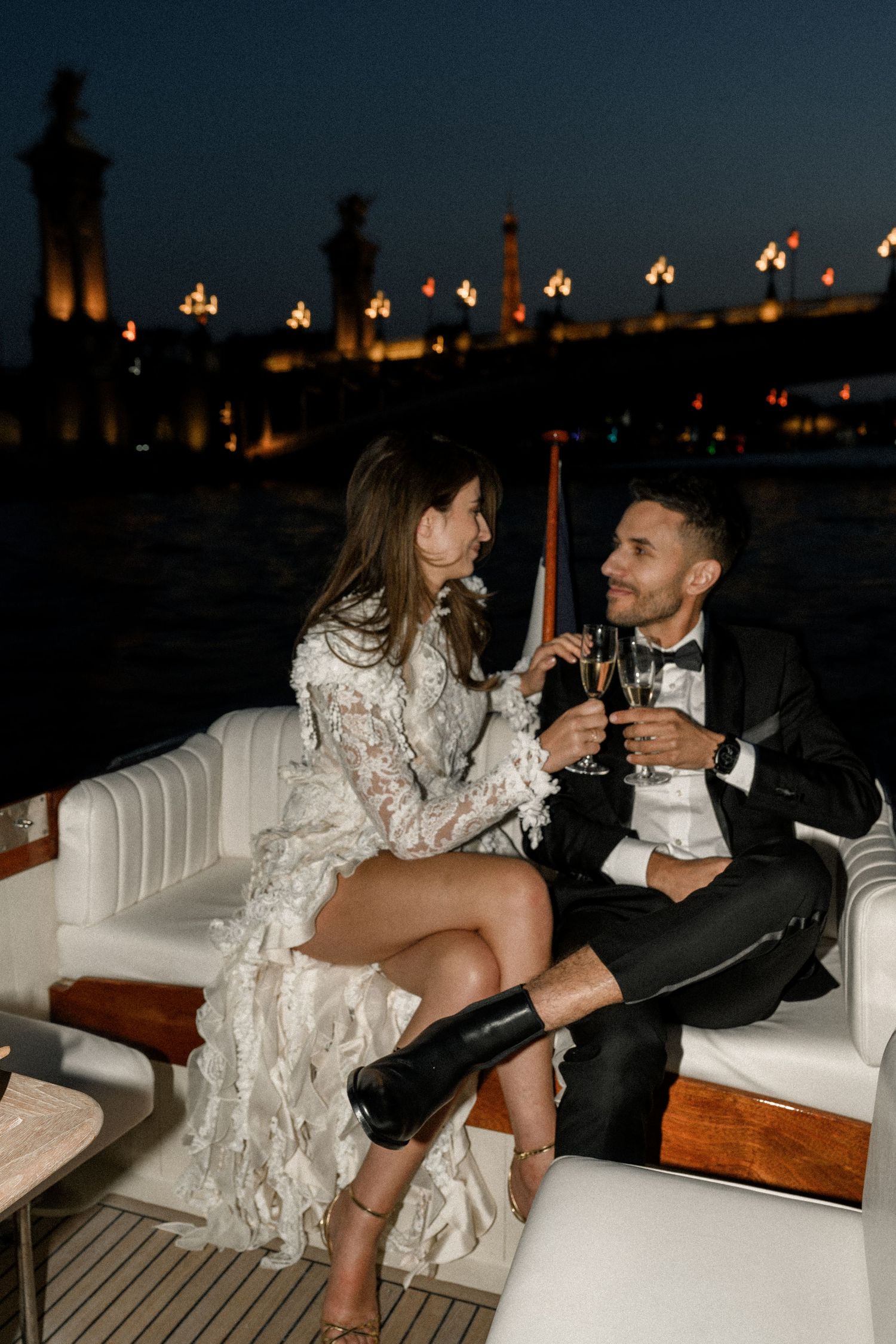 A romantic wedding moment captured on a boat with a stone bridge backdrop in black and white photography.