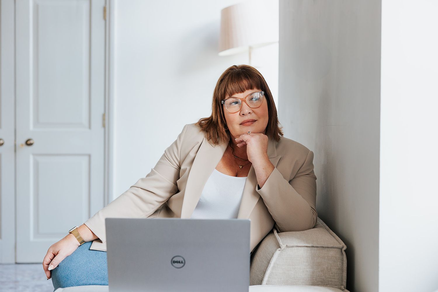 Person in a beige blazer sits thoughtfully with a Dell laptop while working from a comfortable home office setting.