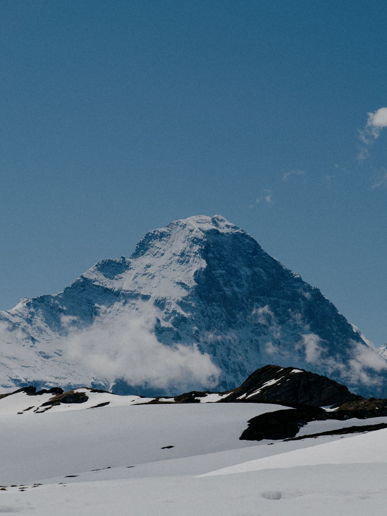Panoramic view of snow-covered mountain peaks against a bright blue sky with wispy clouds.