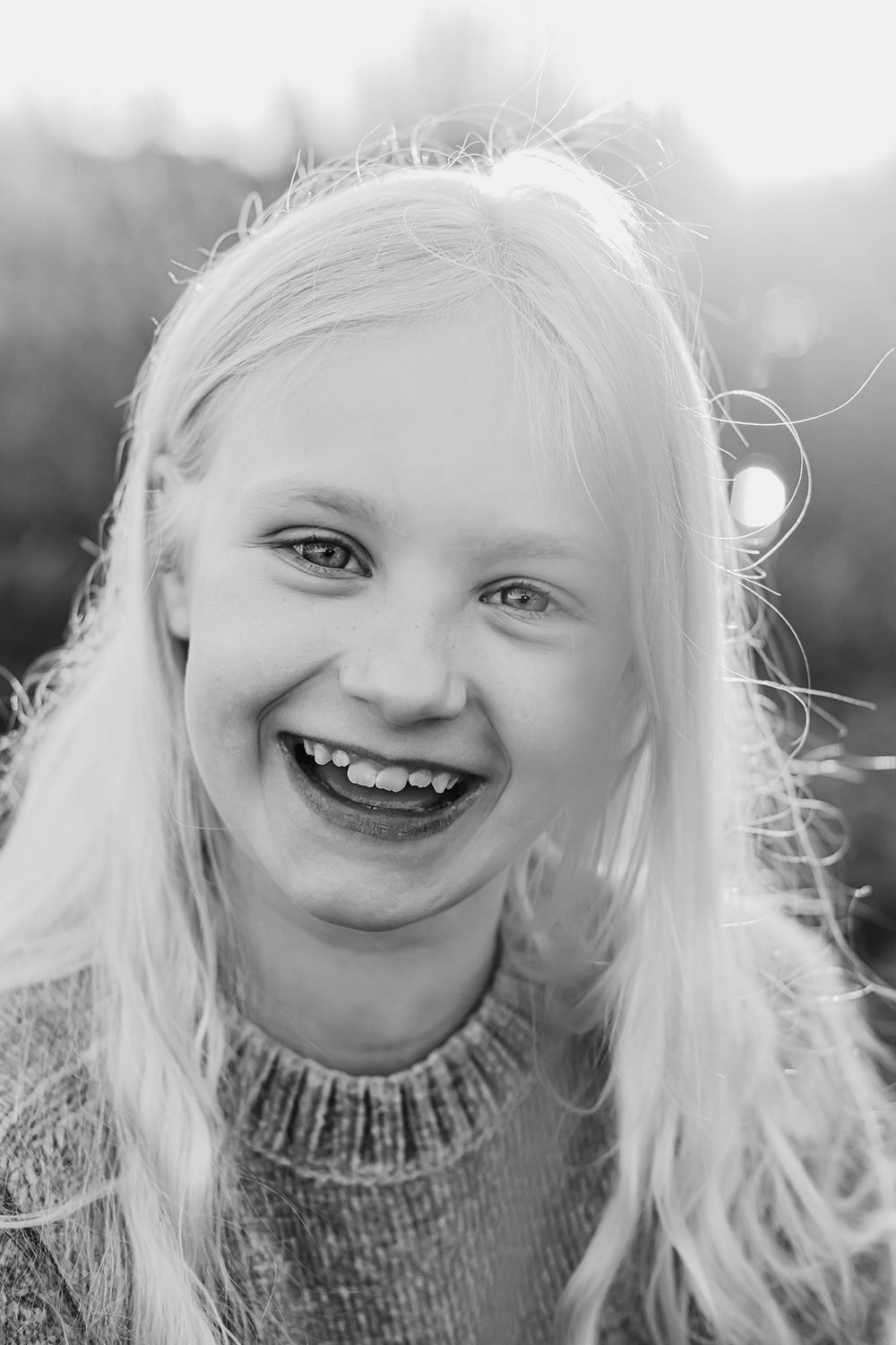 Porträtt med känsla oh stark glädje i en liten flickas ansikte, det är vackert motljus och håret lyser upp. Fotograf Lets Bloom Media.