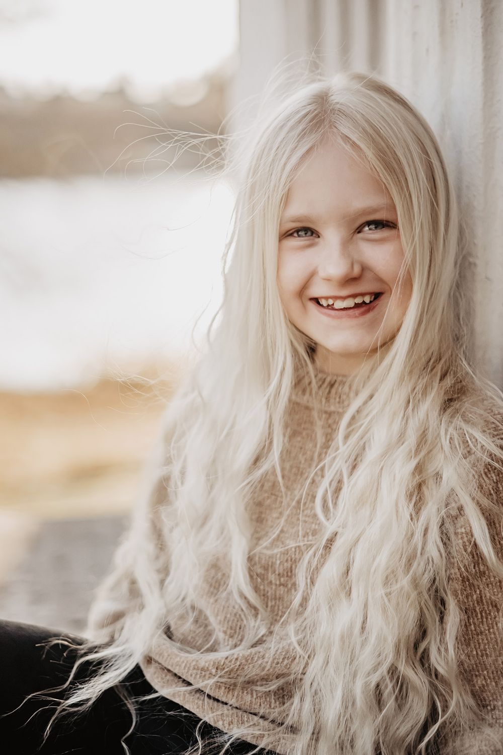 En ung flicka med vackert långt blondt hår sitter vid Lusthuset Lugnet vid stranden i Finspång, hon ler in i kameran. Fotograf Lets Bloom