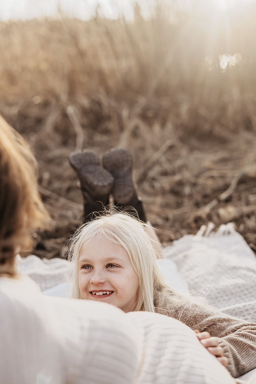 En flicka ligger på mage och tittar på sin mamma intill som är gravid, flickan håller handen på magen och ler. Gravidfotograf Lets Bloom