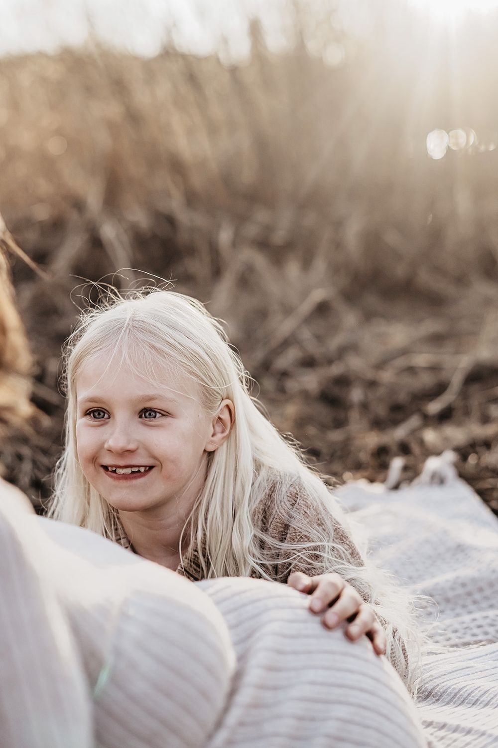 En ung flicka håller sin hand på sin gravida mammas mage, gravidfotografering på stranden med Lets Bloom Media i Östergötland.