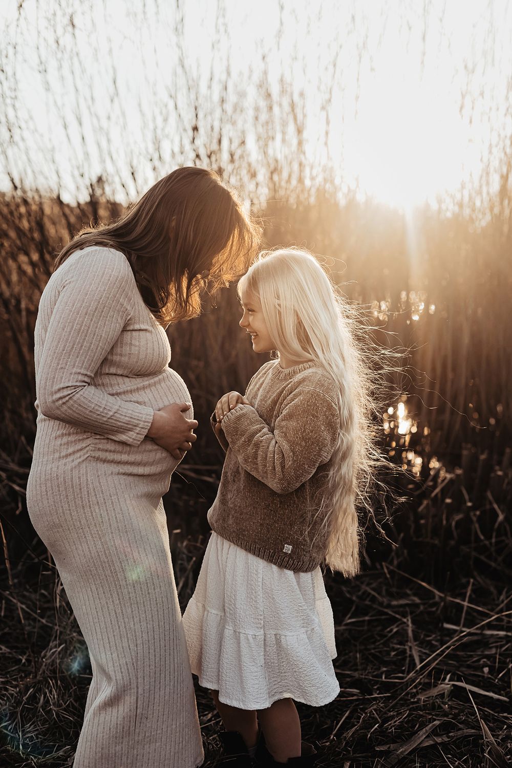 Vackert motljus landar över mor och dotter som står mot varandra, mamman är gravid och dottern skrattar och är lycklig, hennes hår lyser.