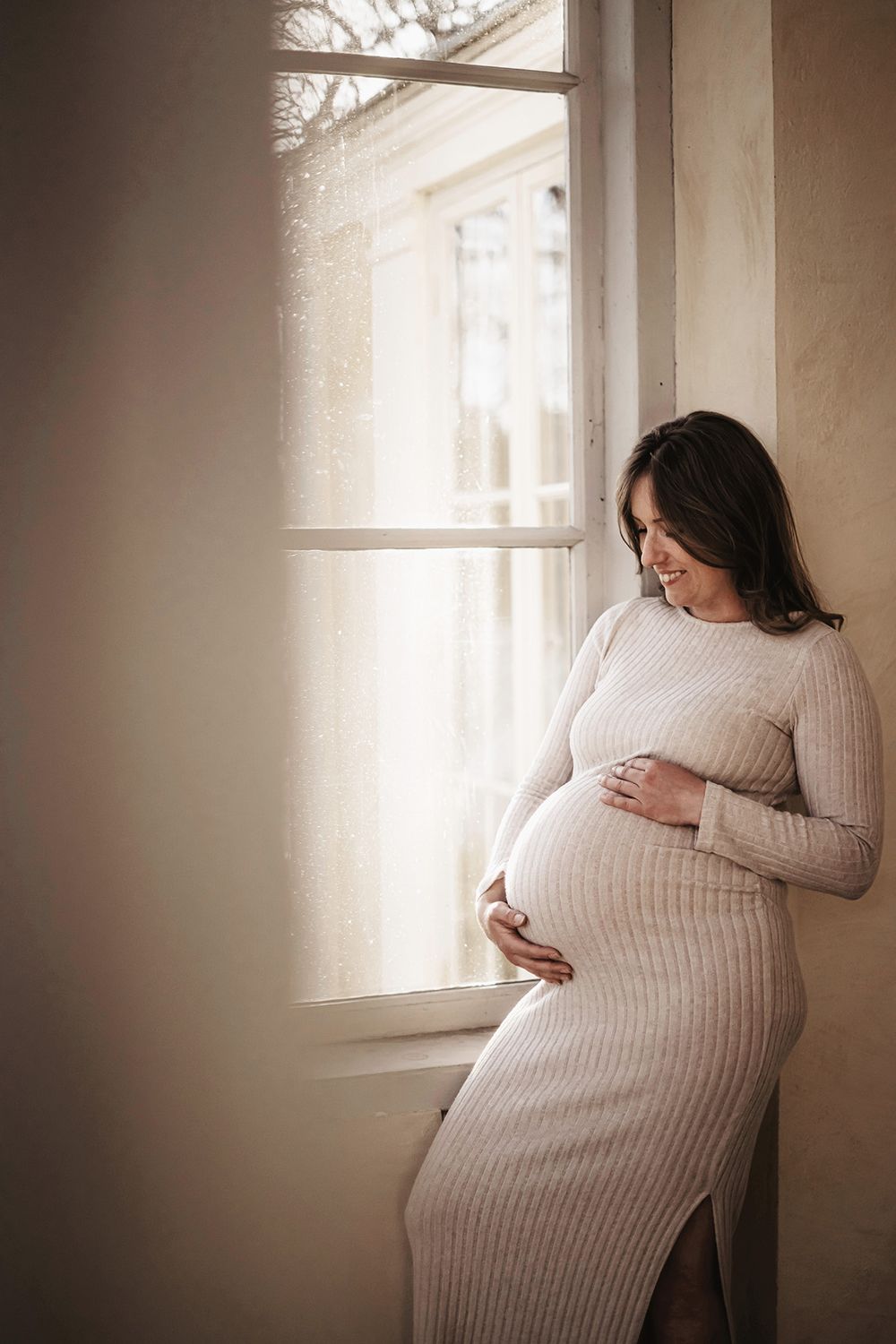 Porträtt på gravid kvinna som står vid ett vackert gammalt fönster vid Lusthuset Lugnet i Finspång. Fotograf Josefin Landhagen Lets Bloom