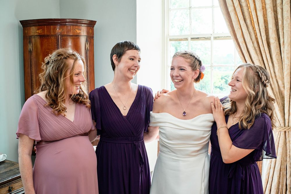 A group of friends share a joyful moment together at a wedding celebration, wearing purple and white dresses.