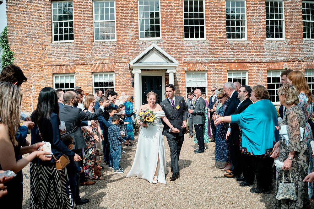 Groups of wedding guests lined up outside a historic brick building during a cheerful reception celebration.