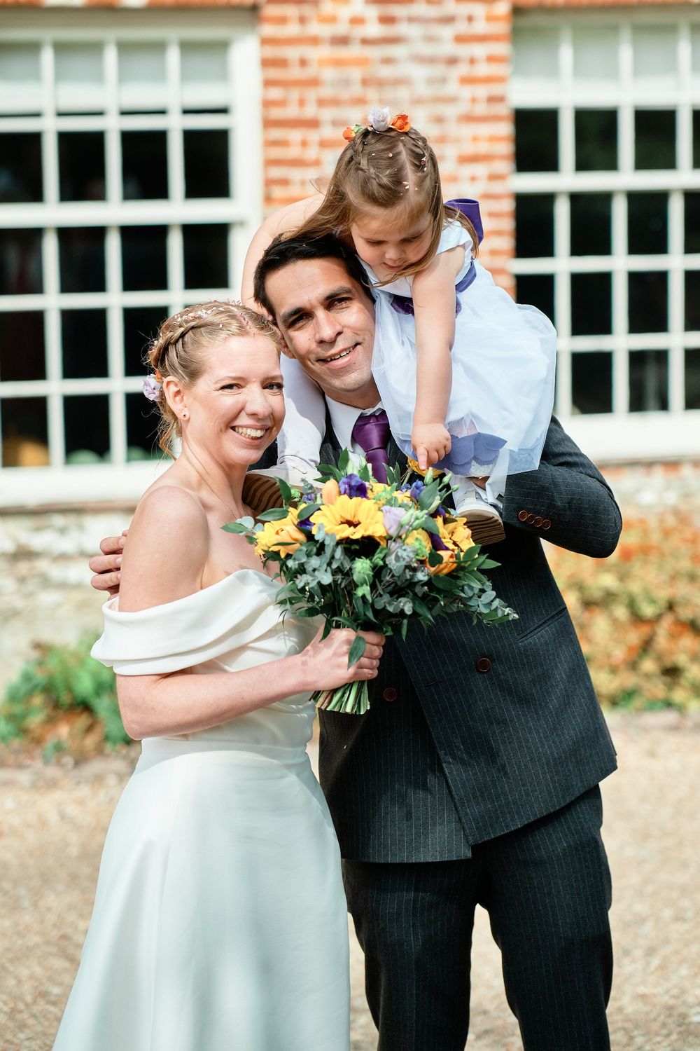 A couple shares joyful wedding moments in front of a brick building, with colorful floral bouquets in hand.
