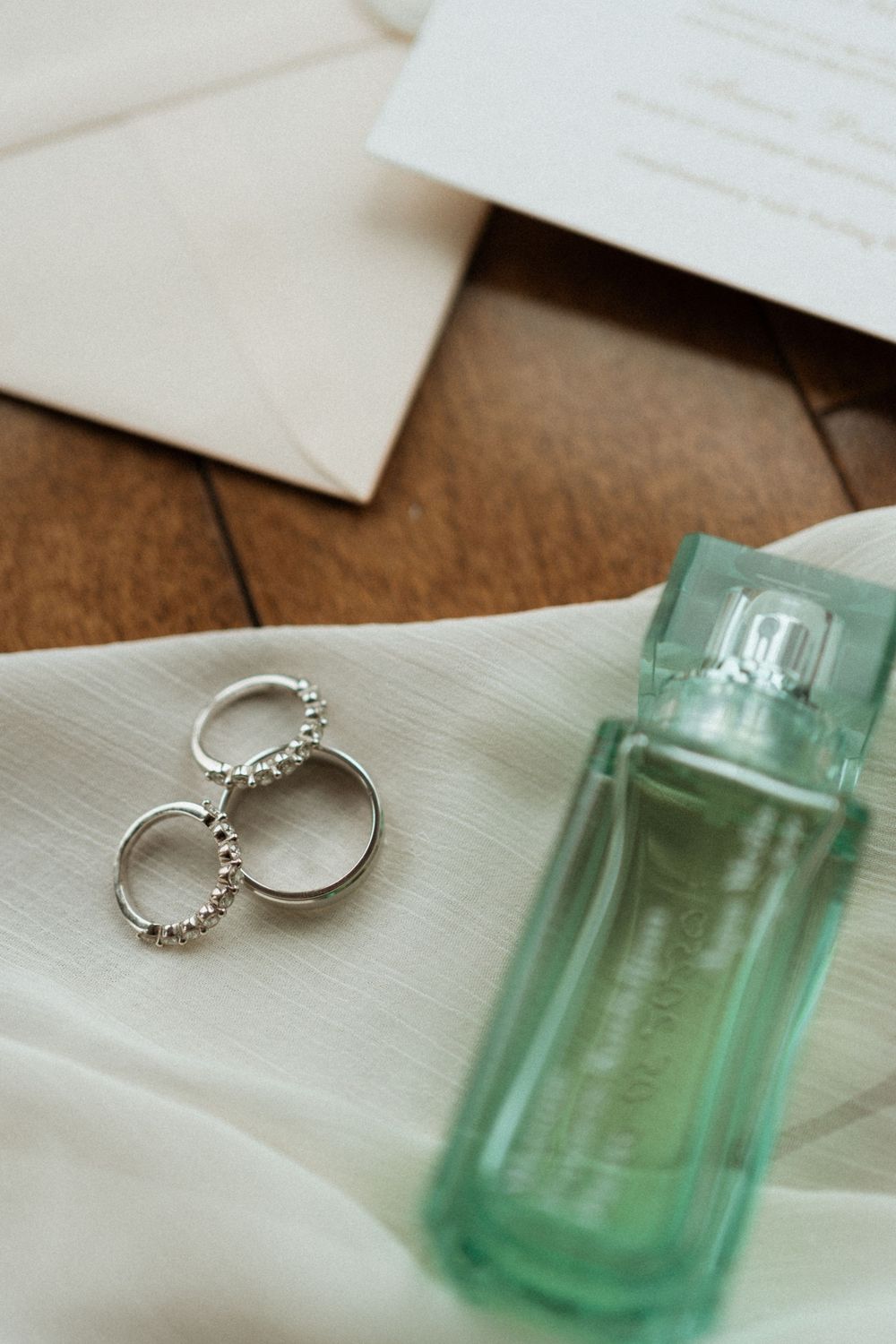 Wedding rings and a light green perfume bottle arranged on white fabric with romantic styling details.