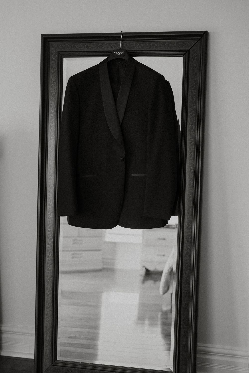 A black suit jacket hangs on display in a black frame against a white wall.