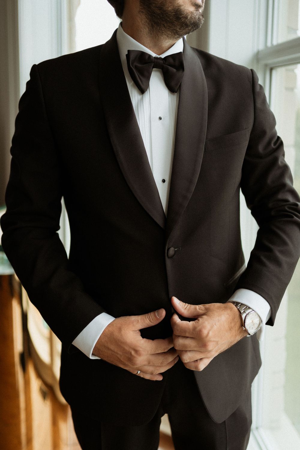 A close-up shot of a classic black tuxedo with bow tie and white dress shirt in natural window light.