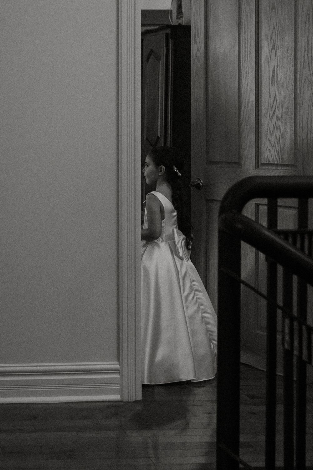 A person in white clothing stands in a dark doorway creating an eerie atmosphere in black and white.