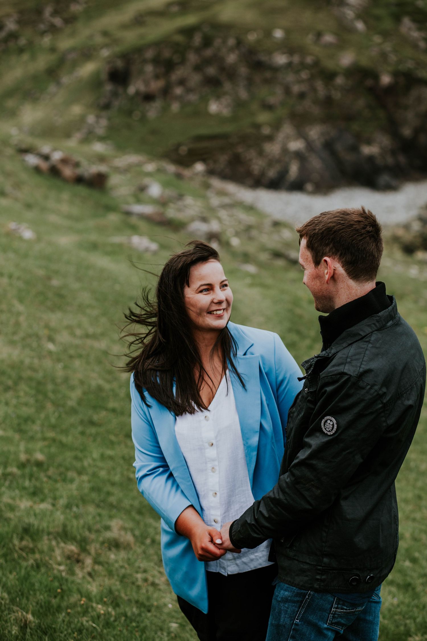 A couple shares a joyful moment on green coastal cliffs overlooking the ocean.