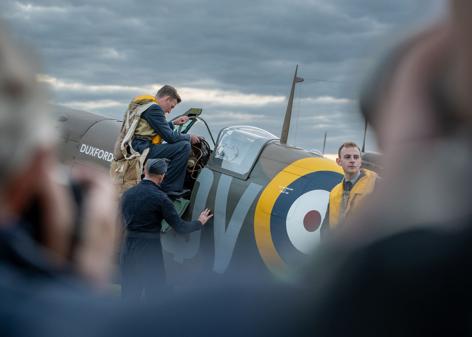 Spectators gathered around a historic RAF Spitfire aircraft during an evening photo shoot.