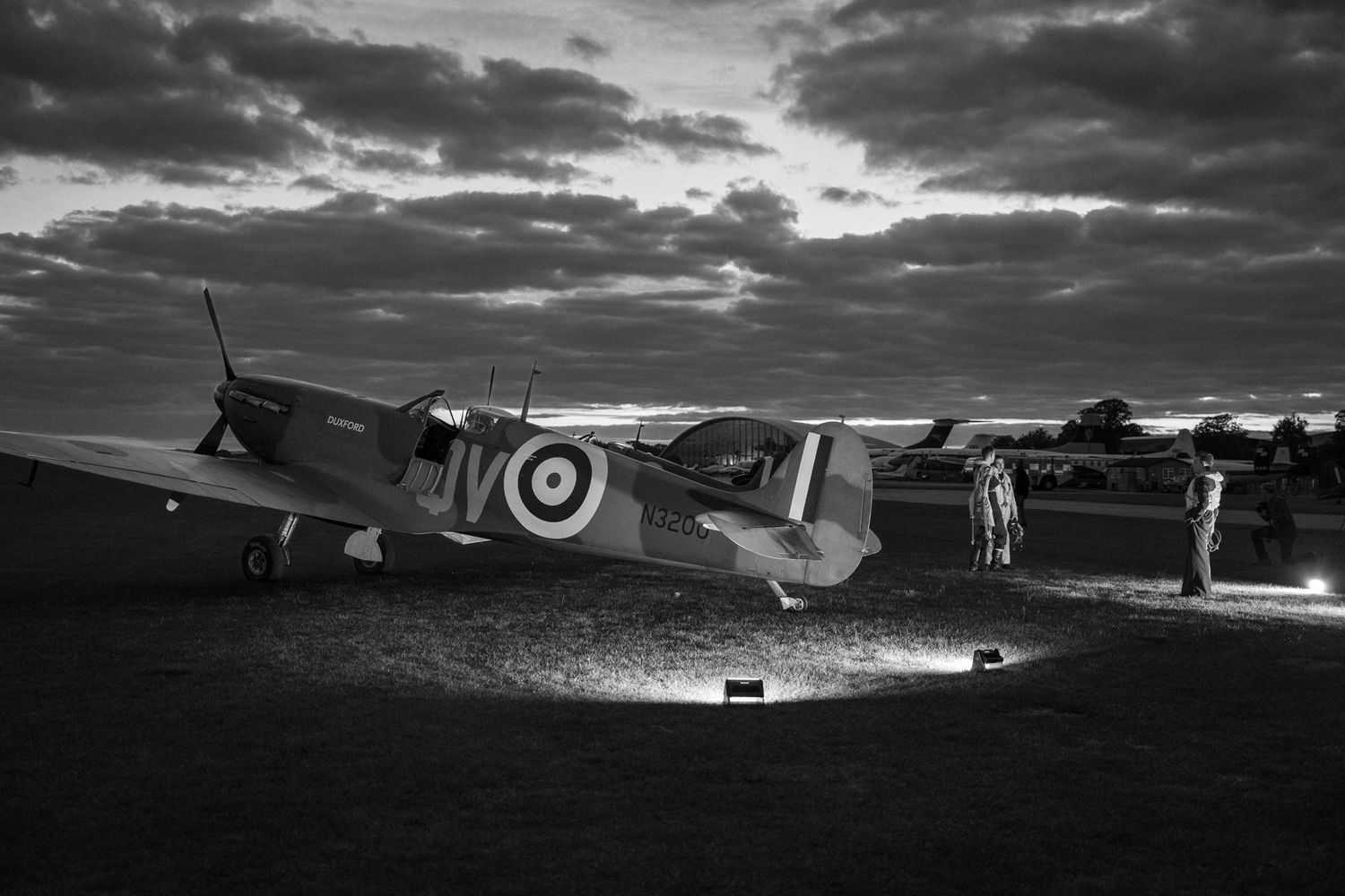 Classic Spitfire fighter plane at rest on darkened airfield under dramatic sky.