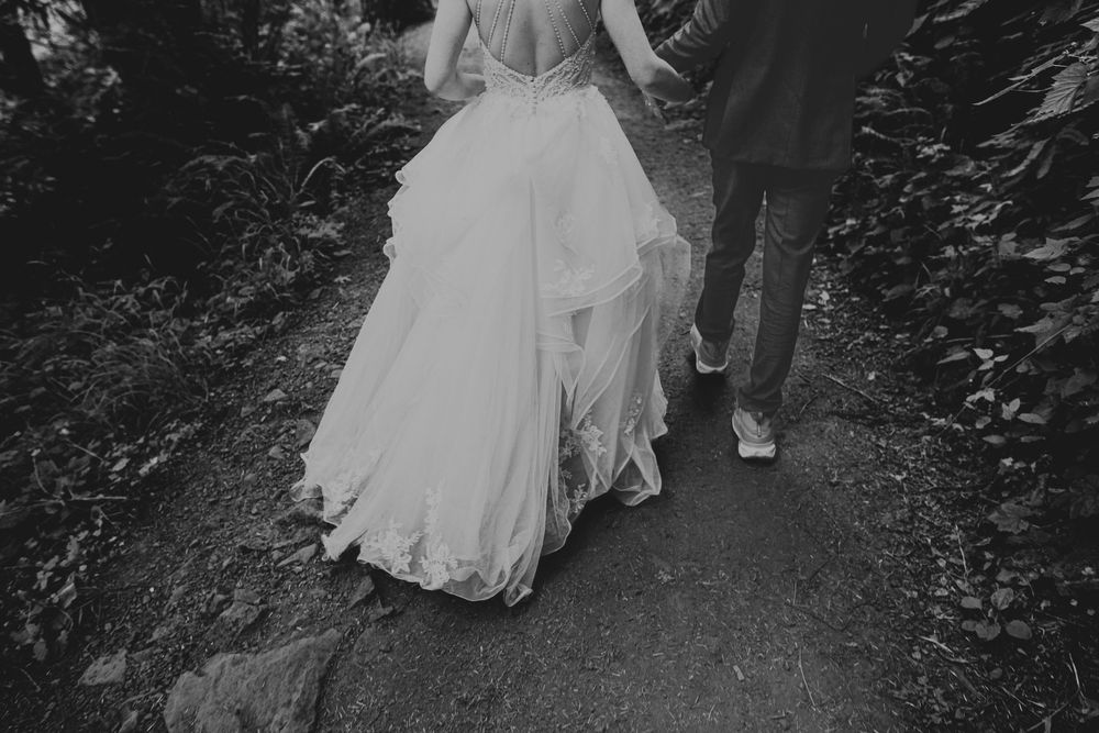 A monochrome view of a wedding couple walking on a garden path, showing only their legs and the bridal gown's flowing skirt.