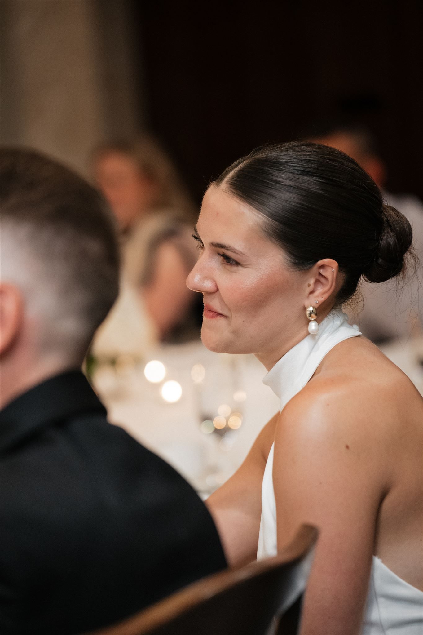 A bride in profile wearing pearl earrings and white gown during a candlelit wedding reception ceremony.