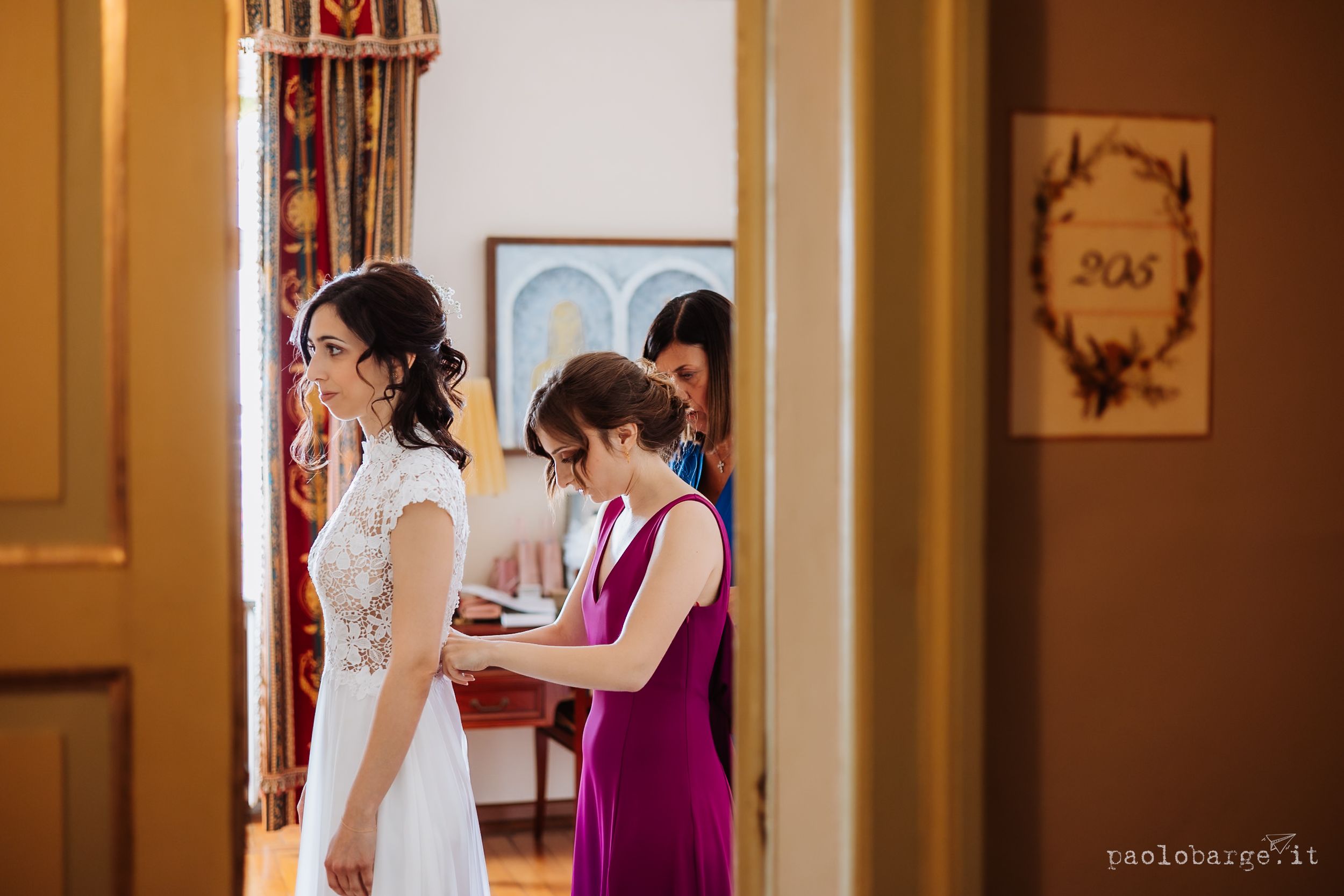 Two people in a classic bridal suite interact in warm lighting with elegant decor visible in the background.