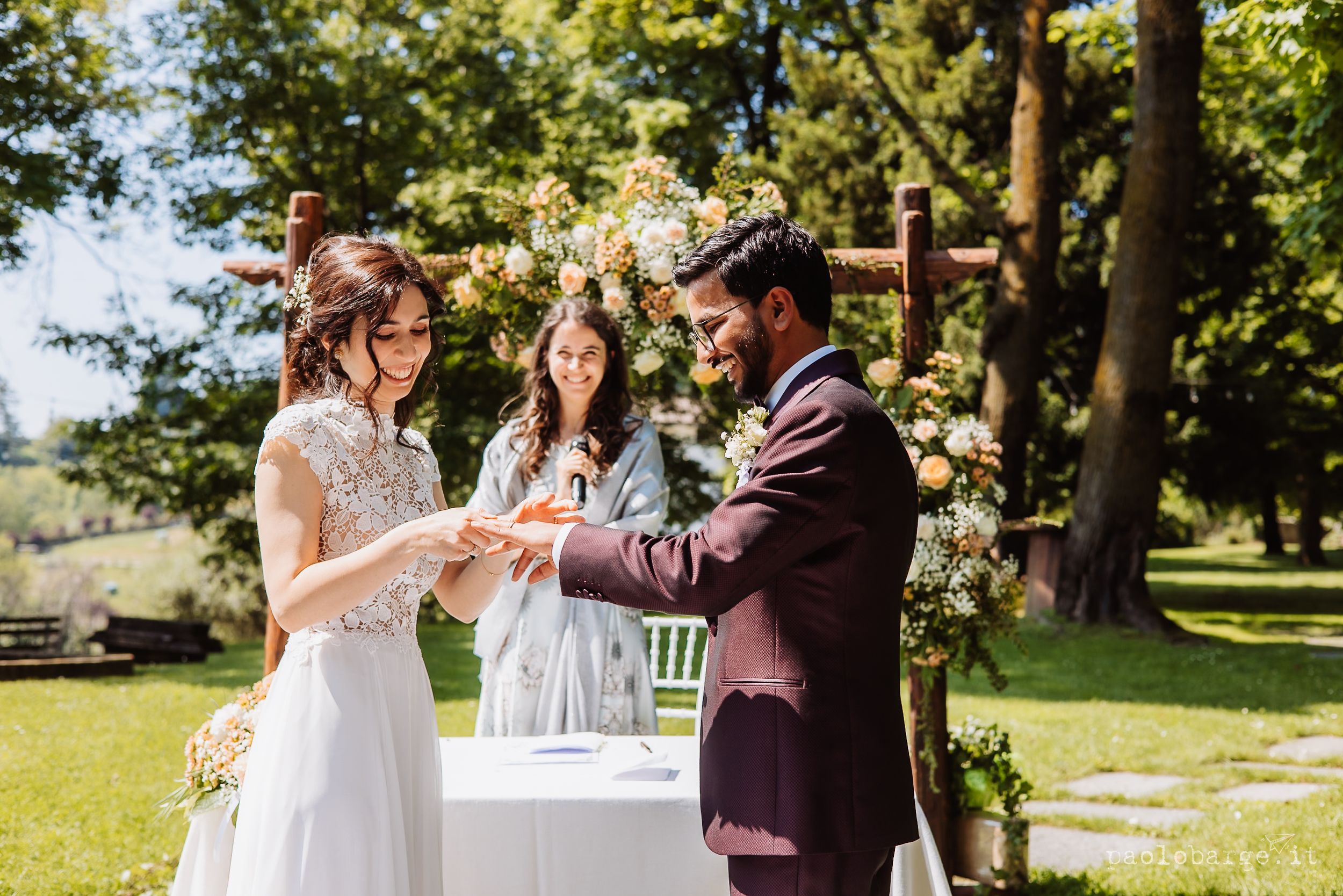 A couple performs a unity sand ceremony during their outdoor summer wedding in a scenic garden setting.