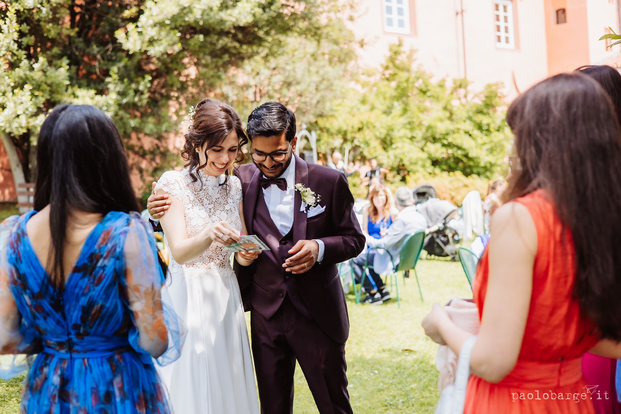 A couple in wedding attire share a moment with guests outdoors in a garden setting.