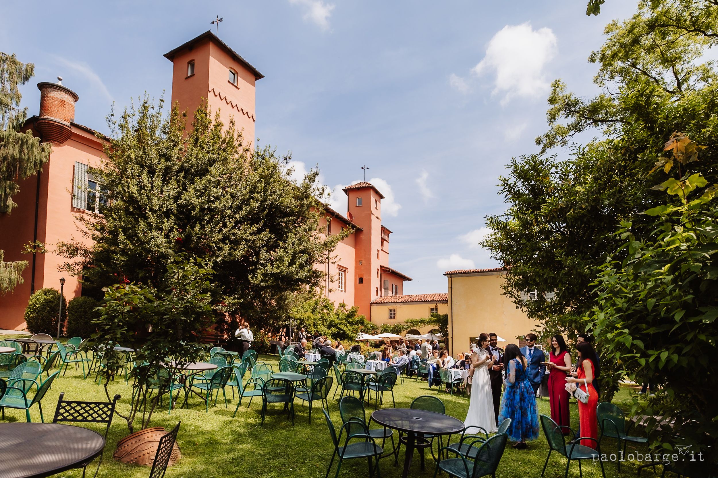 Outdoor garden party setup with green chairs and tables against a rustic red building on a sunny day.