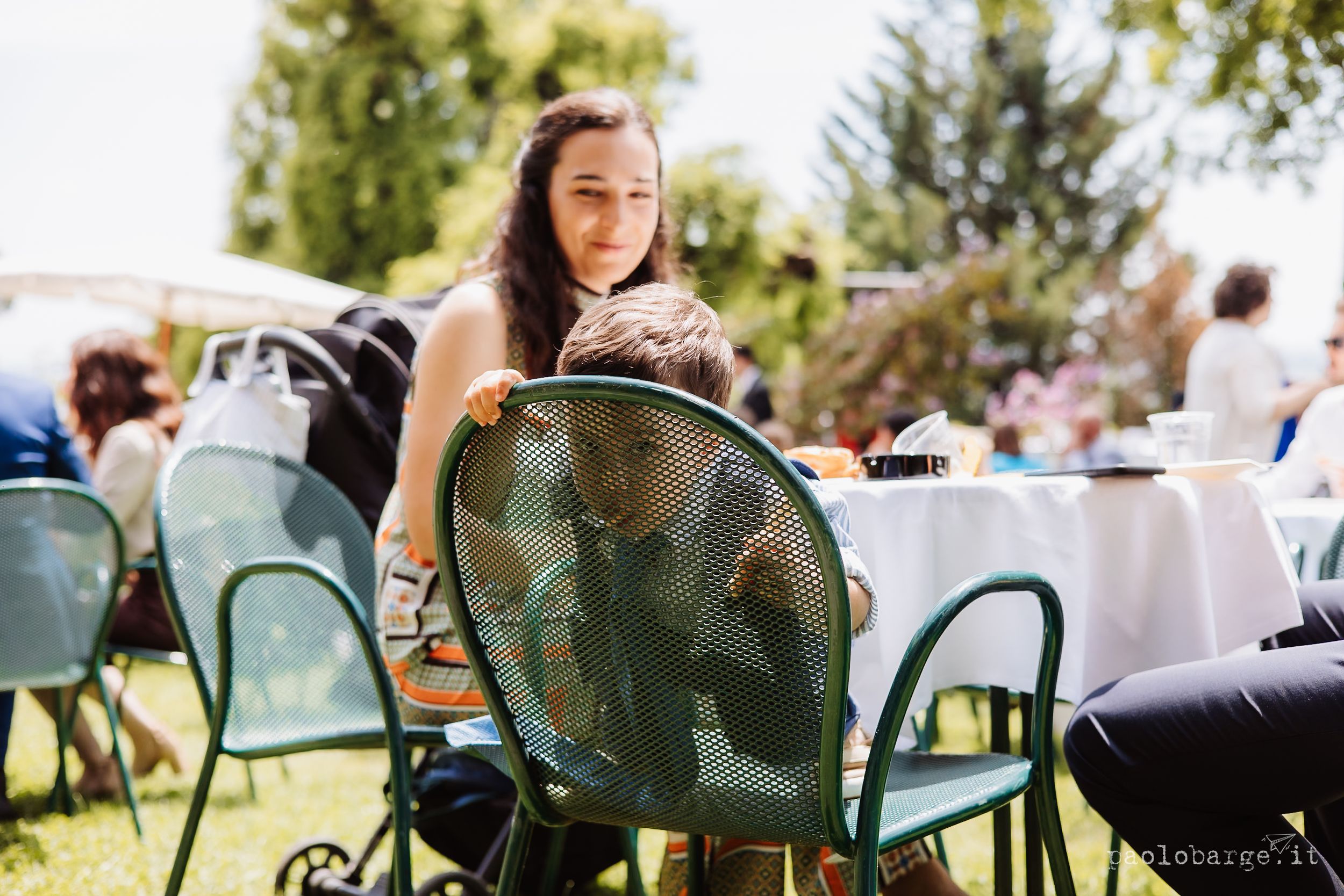Someone relaxes in a turquoise metal chair at an outdoor garden party with tables and chairs set up.