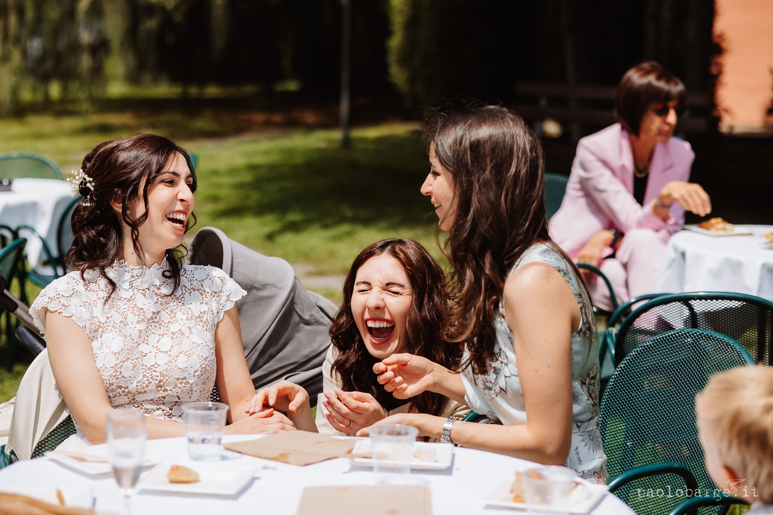 Guests sitting outdoors at wooden tables enjoy casual conversation during a wedding reception.