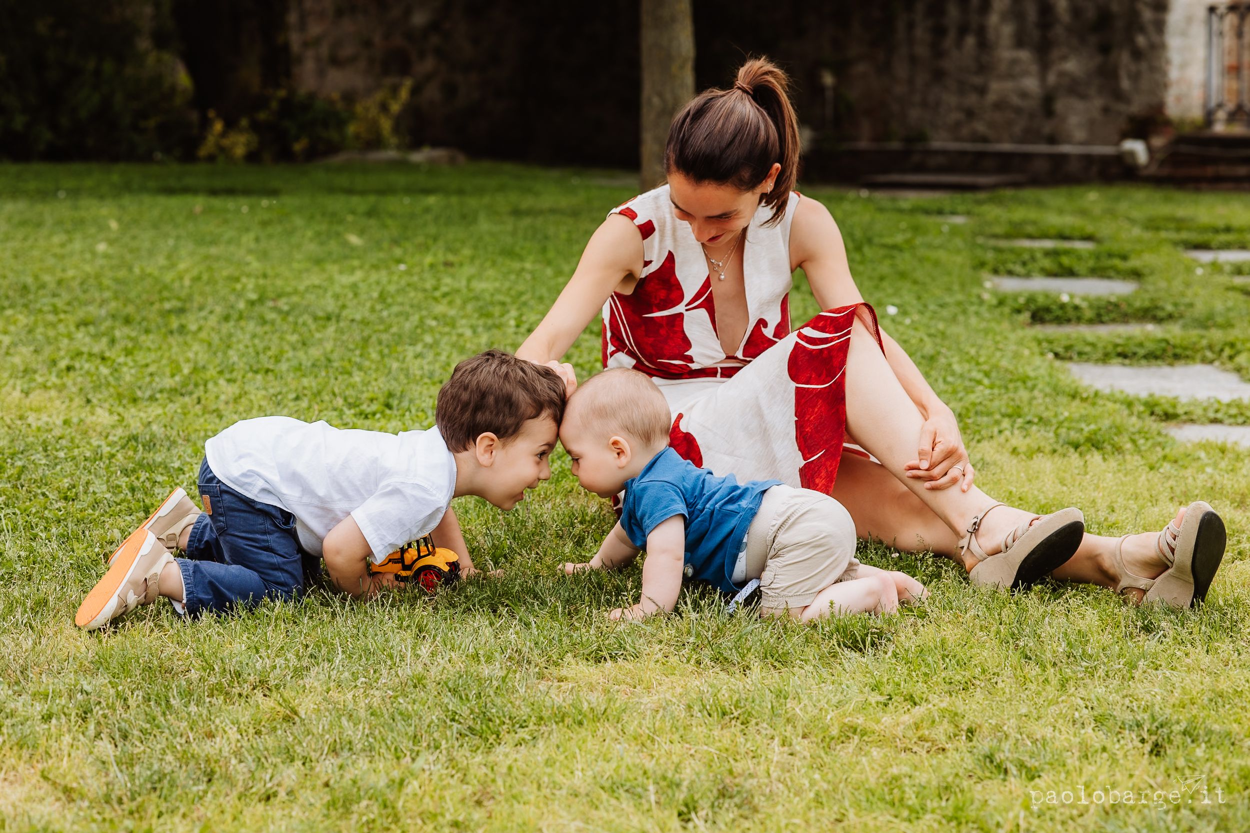 People playing and crawling together on green grass in a playful outdoor scene with stone pathway.