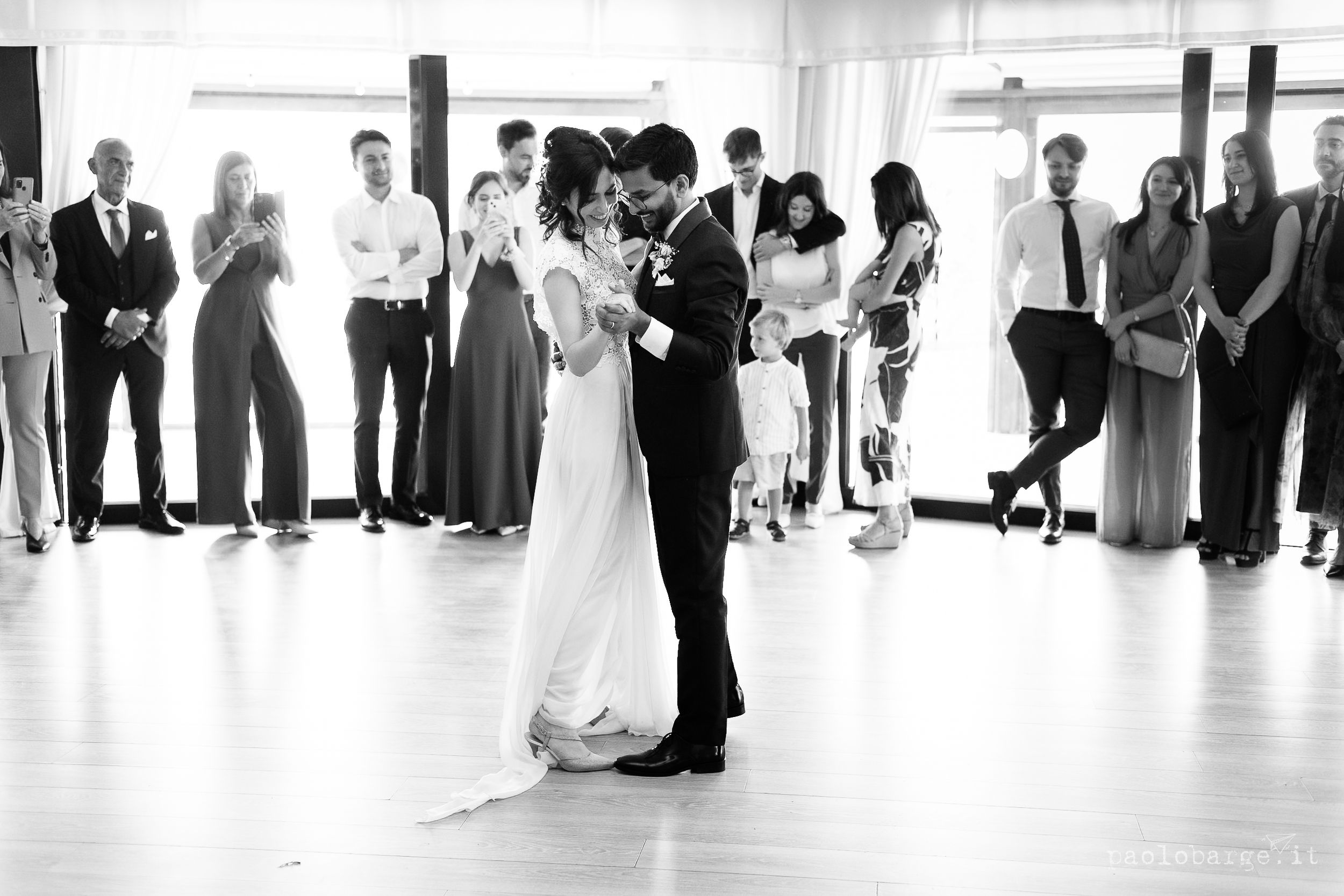 A couple shares their first dance as newlyweds while wedding guests look on at an elegant reception venue.