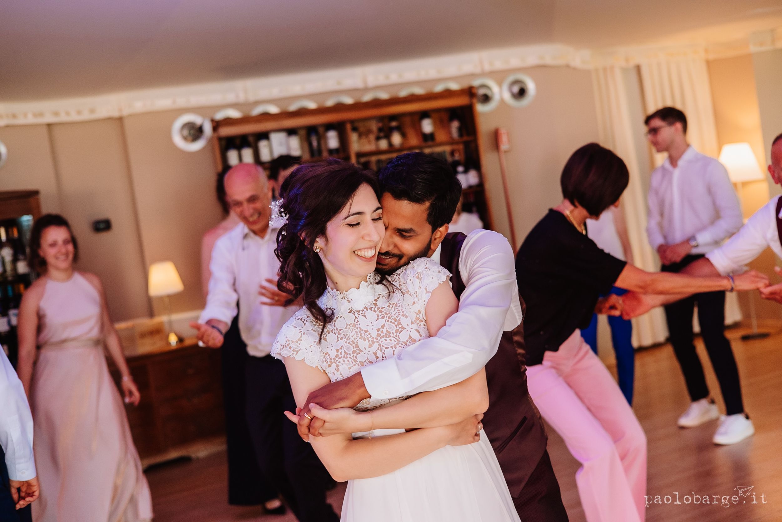 A couple dances close together at a wedding reception while other guests mingle in the background.